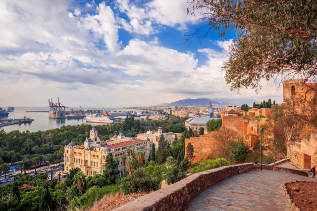 Vista panorámica de la ciudad y el puerto de Málaga con la Alcazaba, edificios históricos y montañas al fondo, Andalucía, España