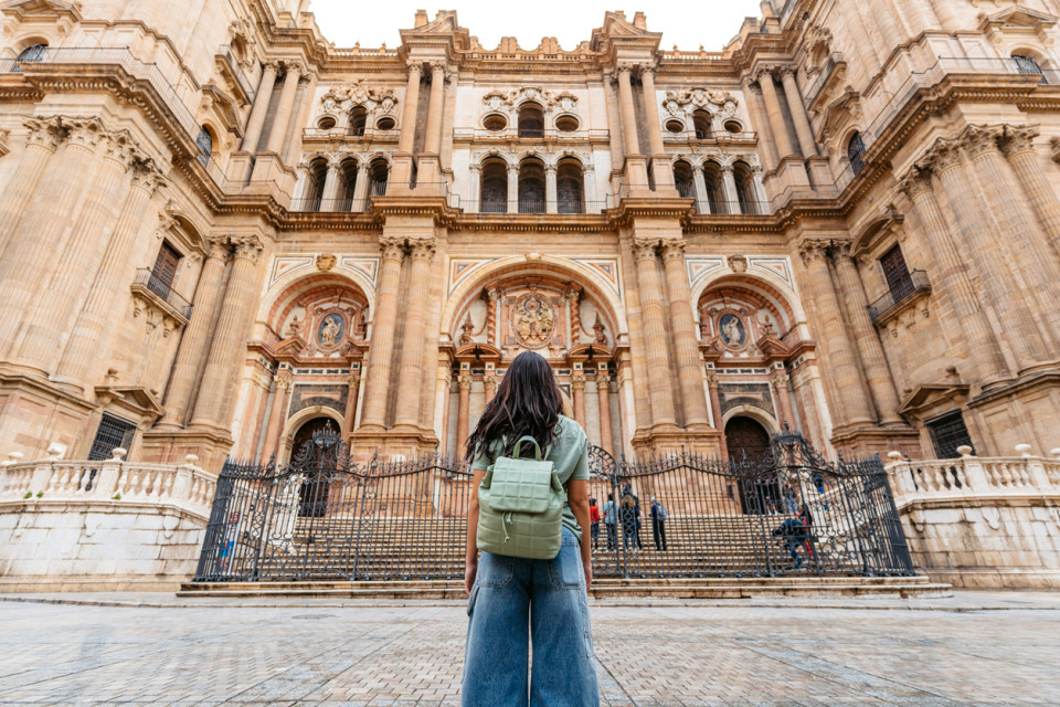 Mujer con una mochila verde admirando la fachada de la Catedral de Málaga, un histórico monumento renacentista en Andalucía, España