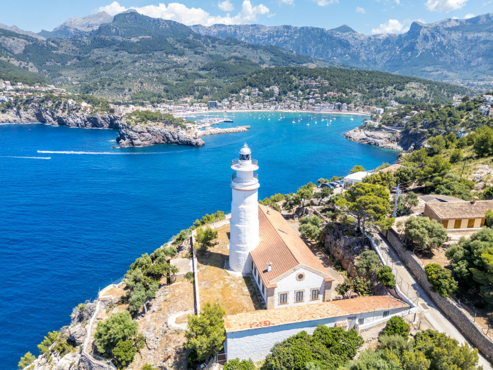 Vista aérea del faro de Port de Sóller con aguas turquesas, yates de lujo y la sierra de Tramuntana en Mallorca.