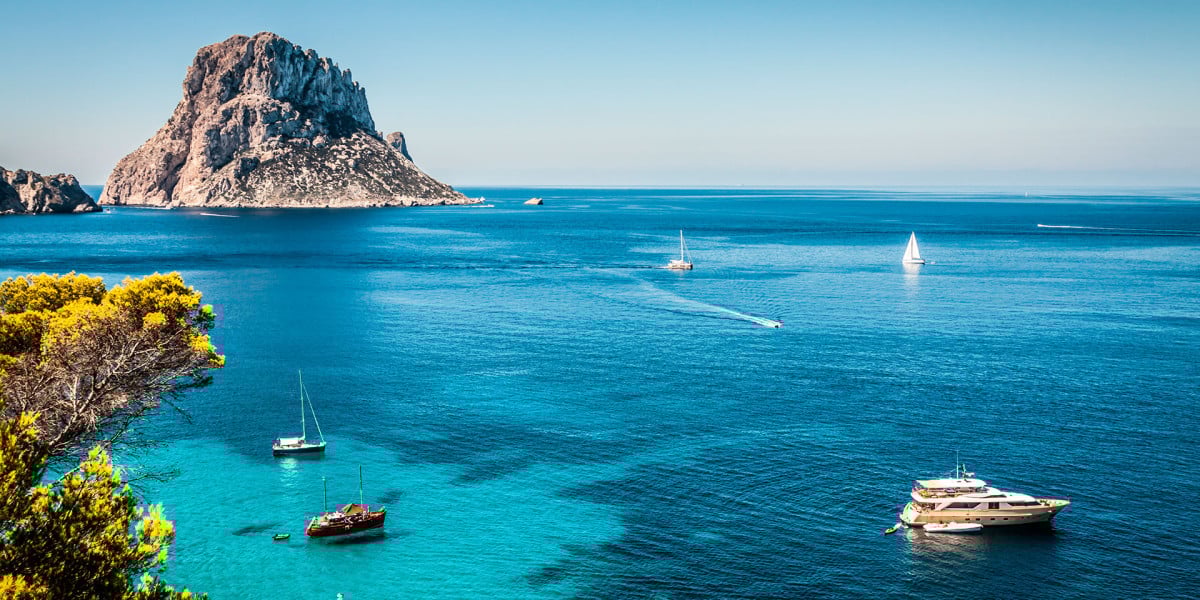 Vista panorámica de Ibiza con el mar azul turquesa, barcos anclados y las rocas típicas de la isla
