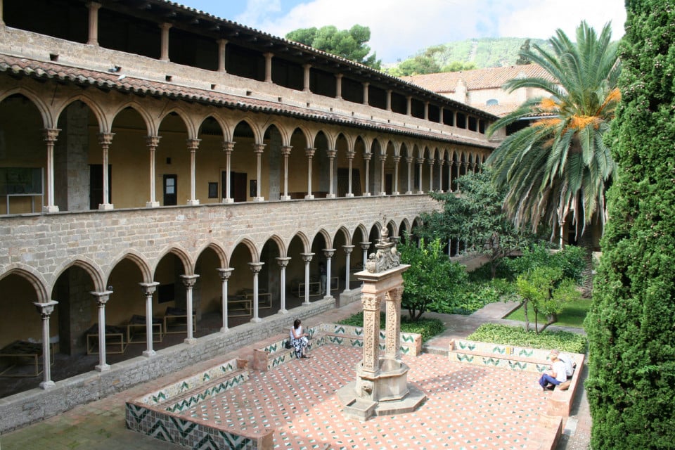 Patio interior del Monasterio de Pedralbes en Barcelona, con arcos góticos, una fuente central y exuberantes jardines mediterráneos.