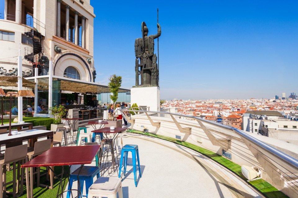 Terraza en azotea de Madrid con vistas panorámicas al centro de la ciudad y estatua icónica, un espacio de ocio cosmopolita.