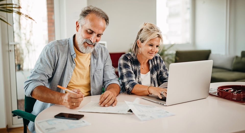 Pareja adulta contemplando costos de hipoteca y post compra de casa sentados en la mesa del living junto con el ordenador